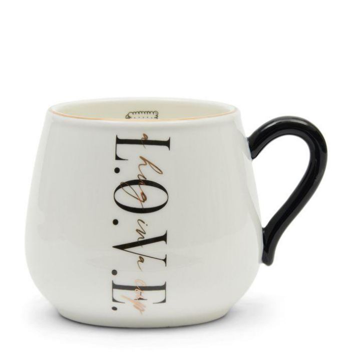 Hug in a Cup Mug Kahvikuppi mustalla tekstilla ja kultakoristeilla.
